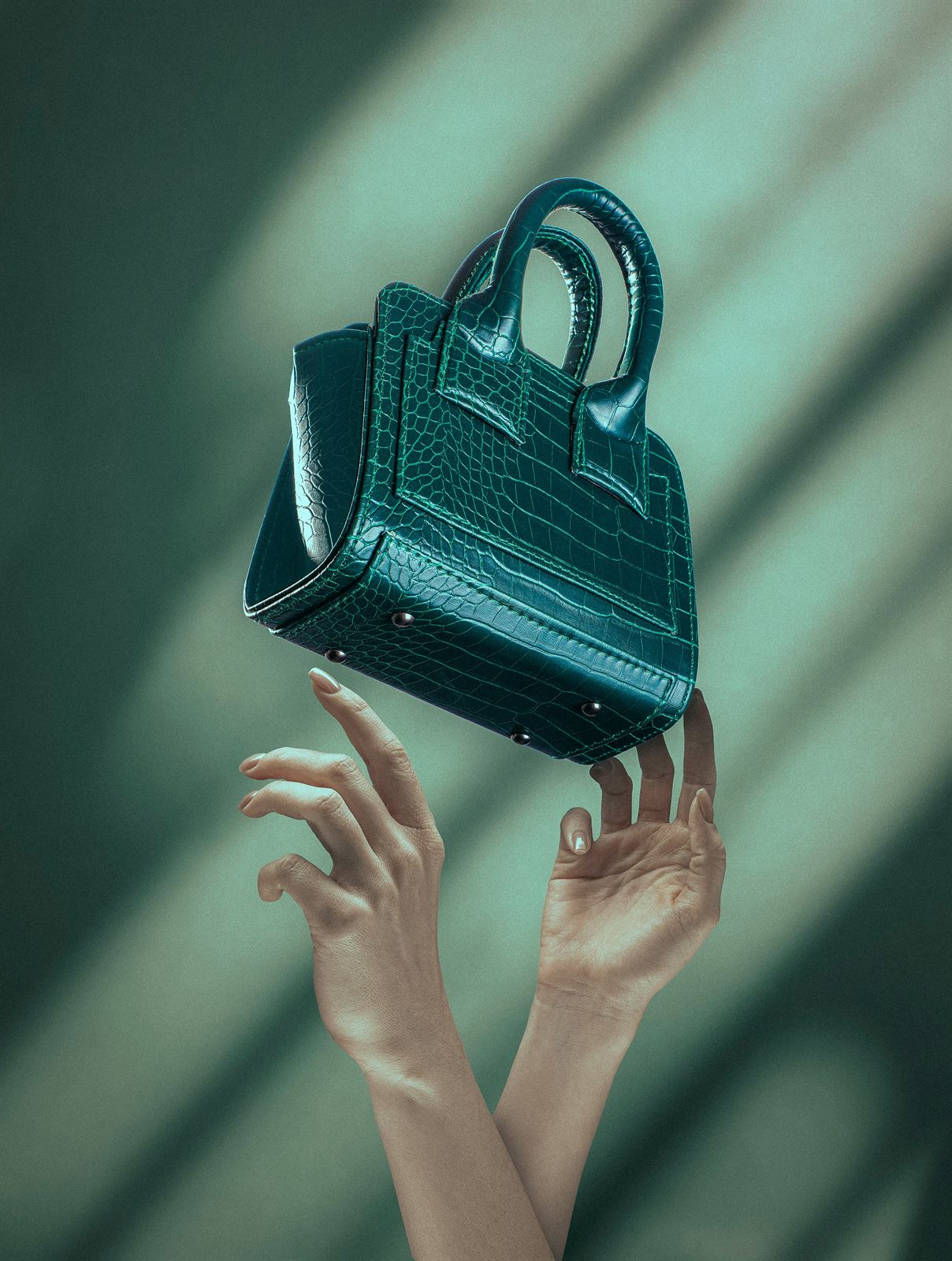 Emerald croc-embossed Verdant mini bag floating above two hands